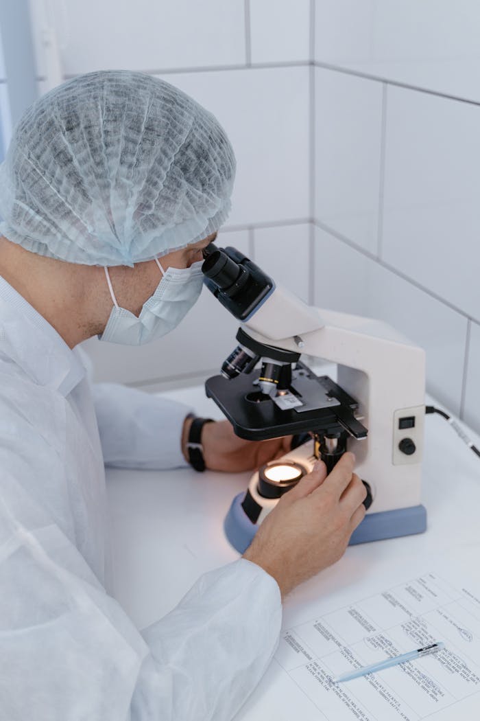 Lab technician in PPE examines samples under a microscope for scientific research.